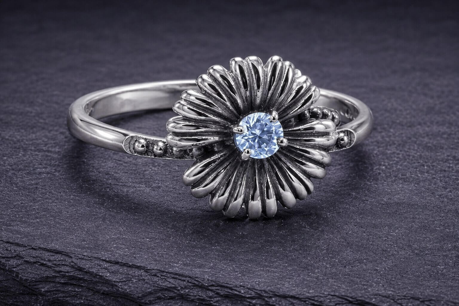 Sterling silver daisy ring with blue cubic zirconia center stone and detailed curved petal design